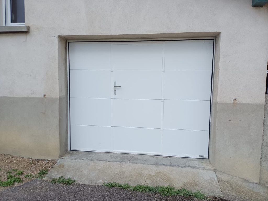 Porte de garage blanche à panneaux verticaux pleins, avec poignée sur le côté gauche, dans une façade beige.