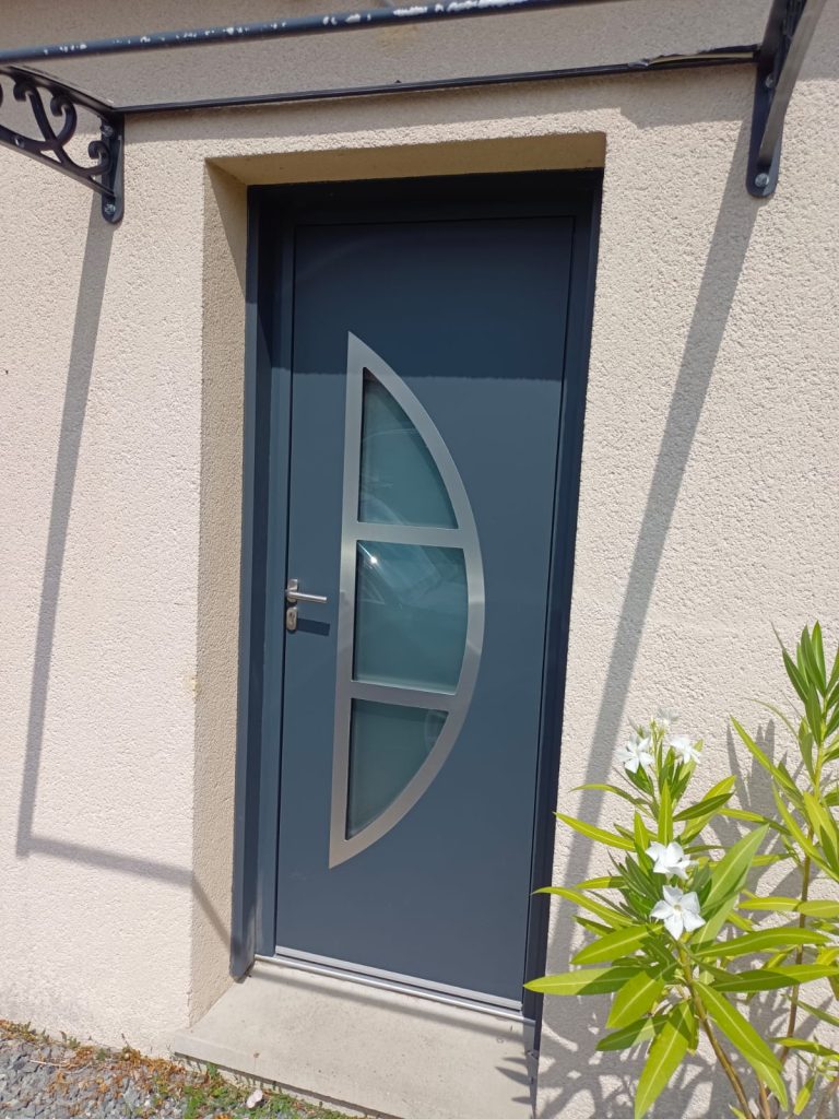 Porte d’entrée gris anthracite avec trois vitrages décoratifs et un encadrement courbe argenté, sur une façade beige.