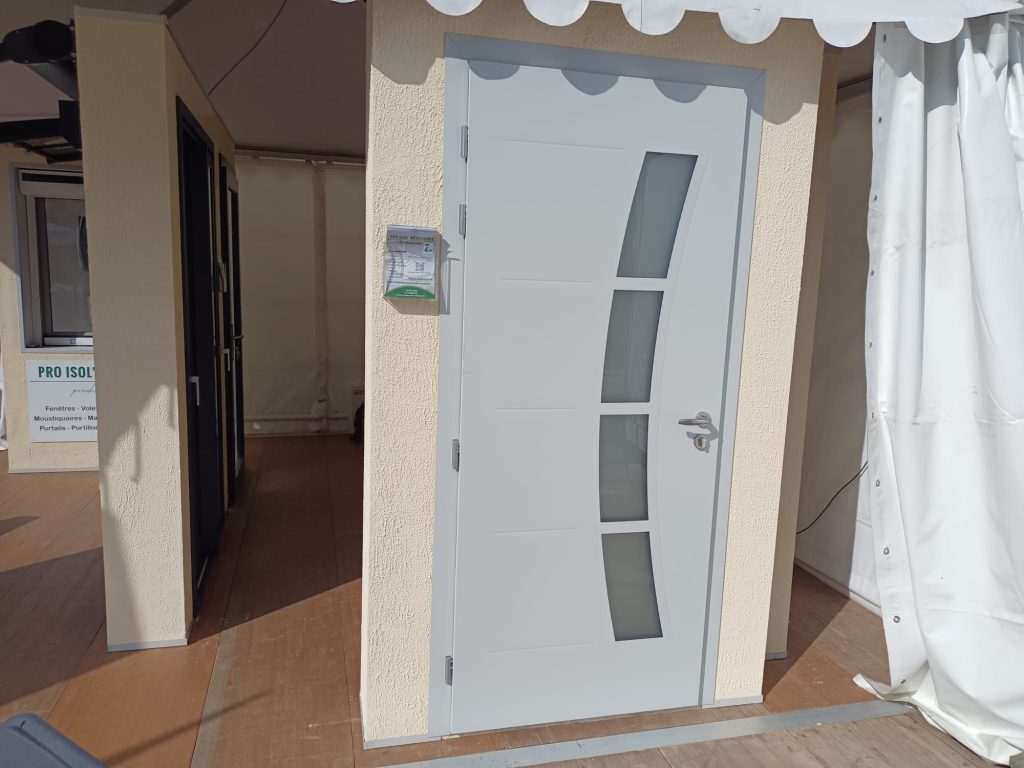 Porte d’entrée gris clair avec quatre vitrages alignés en courbe et une poignée argentée, présentée en exposition.