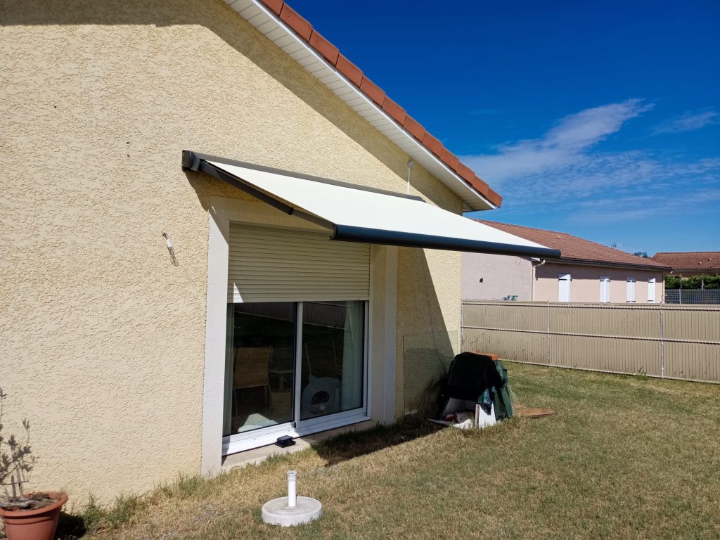 Store banne à toile claire et armature gris anthracite, déployé au-dessus d’une baie vitrée sur une façade beige.