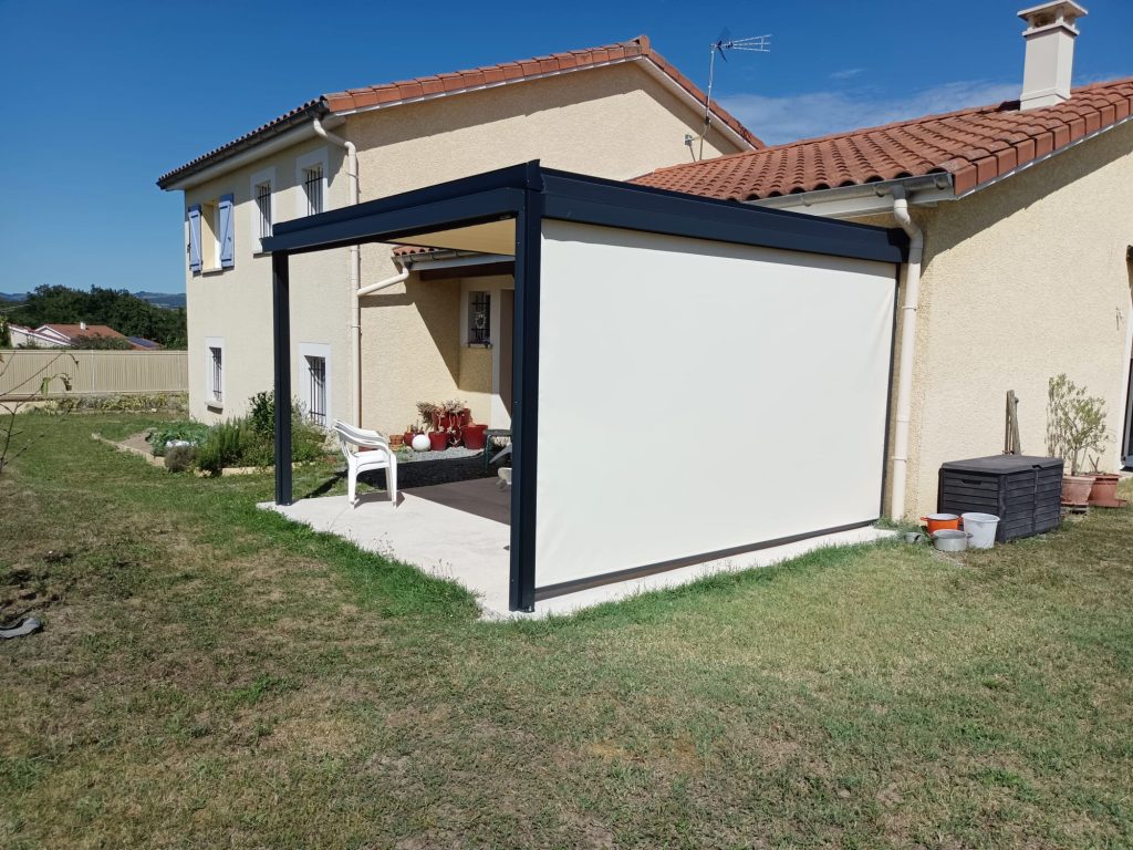 Pergola adossée gris anthracite avec store latéral beige déployé, couvrant une terrasse ouverte sur le jardin.