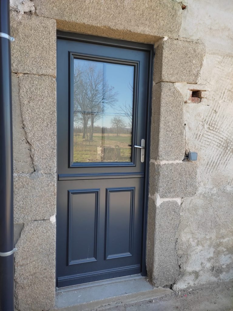Porte d’entrée gris anthracite avec grand vitrage supérieur et deux panneaux moulurés en partie basse, dans un encadrement en pierre.