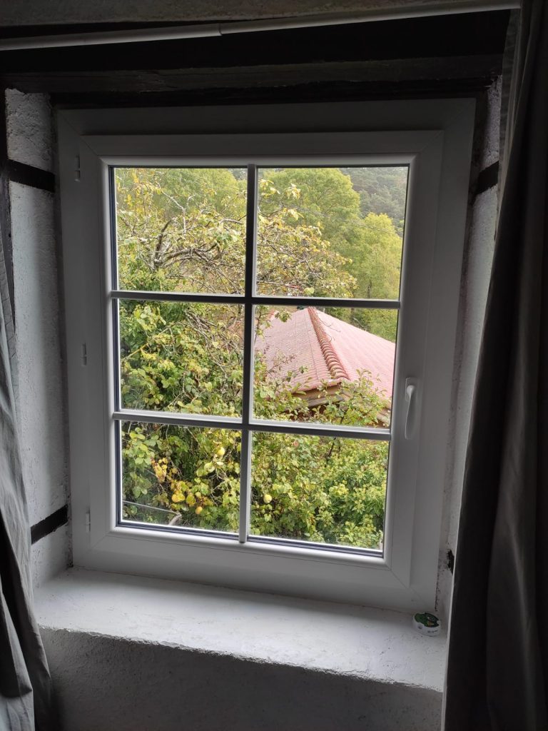 Fenêtre blanche à un vantail avec petits-bois formant six carreaux, vue de l’intérieur avec vue sur les arbres.