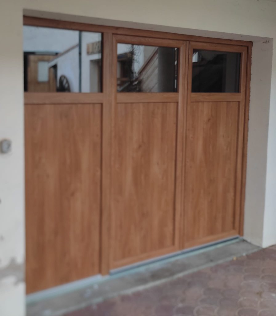 Porte de garage aspect bois composée de trois panneaux, avec vitrages rectangulaires en partie haute.