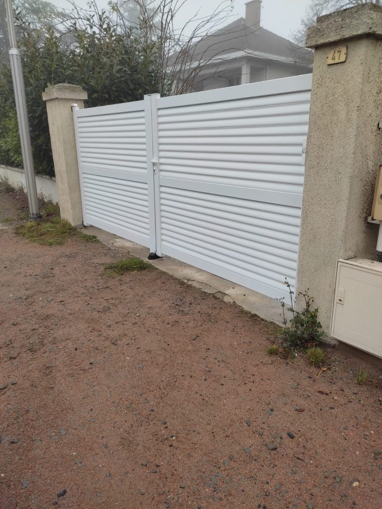 Portail battant blanc à deux vantaux et lames horizontales, installé entre deux piliers maçonnés.