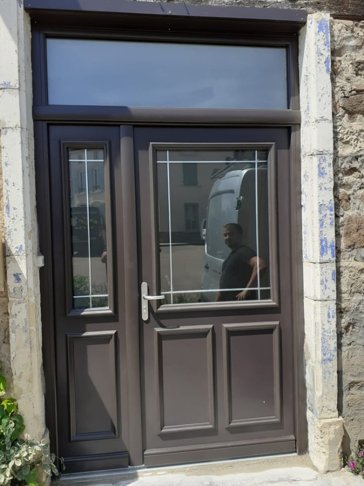 Porte d’entrée brune vitrée à panneaux moulurés, avec partie latérale vitrée et imposte, dans un encadrement en pierre.